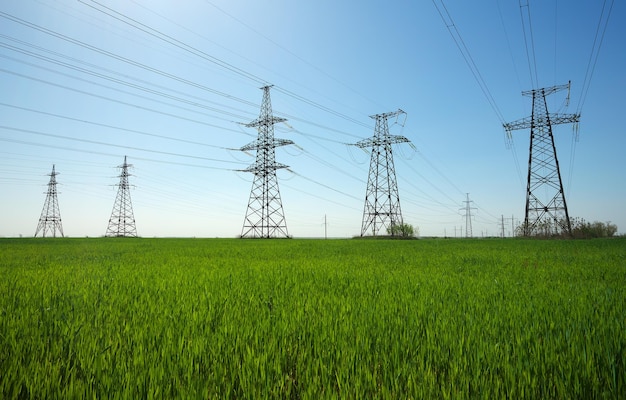 青い空に雲がある晴れた日の平らで緑の農業風景の高圧線と送電鉄塔