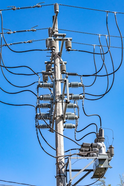 High voltage pole with its electric cables conductors valves and insulators against a blue sky in the background sunny day seen from a lower perspective