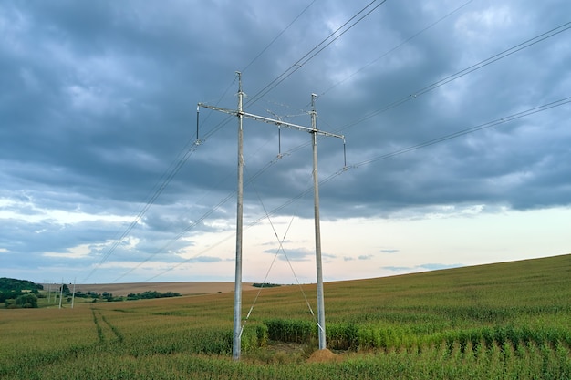 High voltage tower with electric power lines between green agricultural fields. Transfer of electricity concept.