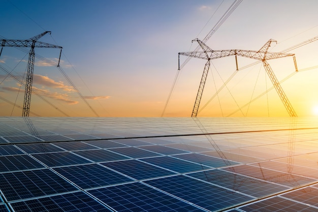 Torri ad alta tensione con linee elettriche che trasferiscono energia da pannelli solari fotovoltaici al tramonto. produzione del concetto di elettricità sostenibile.