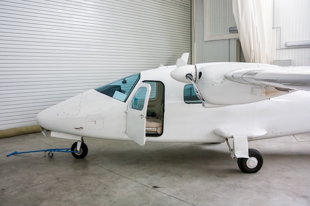 High-winged twin-engined light aircraft with open door in hangar