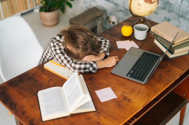 Photo highangle view of tired little child school girl sleeping at work desk lying on notebooks exhausted