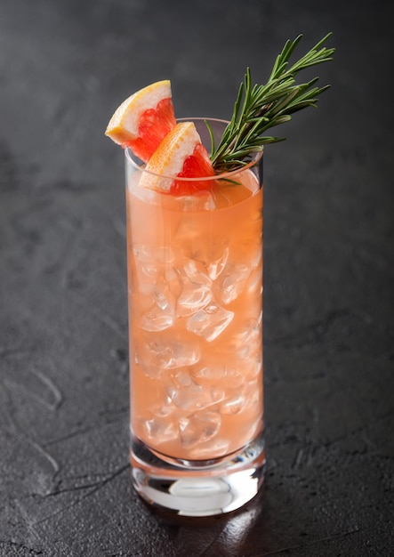 Highball glass of cocktail with red grapefruit and gin with vodka with ice cubes fruit slice and rosemary on black background