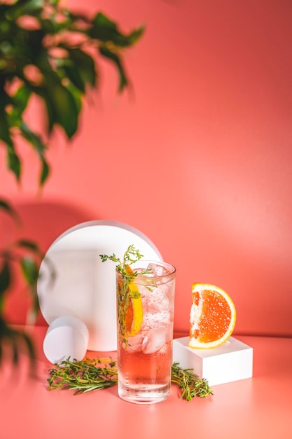 Photo highball glass of fresh grapefruit cocktail with ice rosemary and thyme on pink table surface spring summer art drink food concept