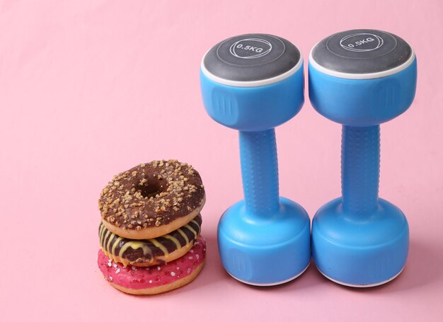 Highcalorie donuts and dumbbells on a pink background losing\
weight fitness concept