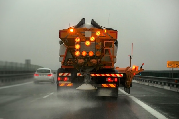 highway maintenance gritter truck spreading de-icing salt, on the ice covered asphalt road during overcast day