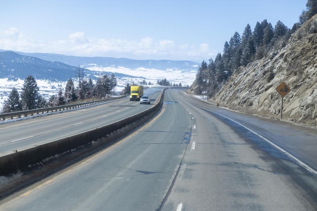 A highway in the mountains with a yellow truck on the right.