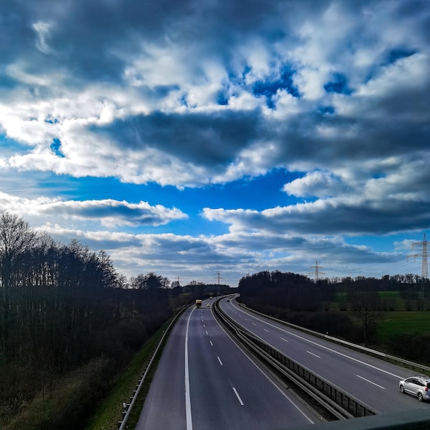 A highway with a car on it and a cloudy sky in the background.