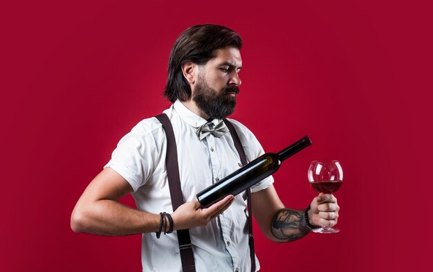Foto hij biedt de beste elegante mannelijke barman knappe hipster drinken wijn glas sommelier proeven van alcohol bebaarde man in bretels drink rode wijn brutale kerel barman in vlinderdas