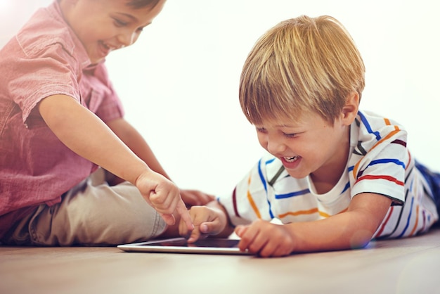 Hij heeft zoveel plezier online Shot van twee kleine jongens die samen een digitale tablet gebruiken terwijl ze op de grond zitten