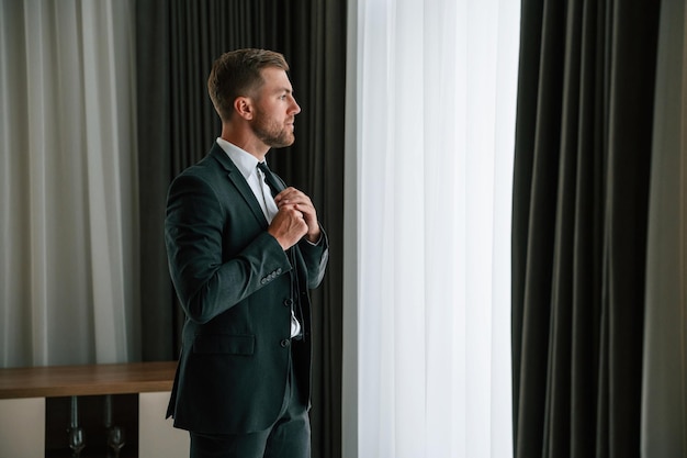 Hij repareert de stropdas. De zakenman is binnen in de hotelkamer.