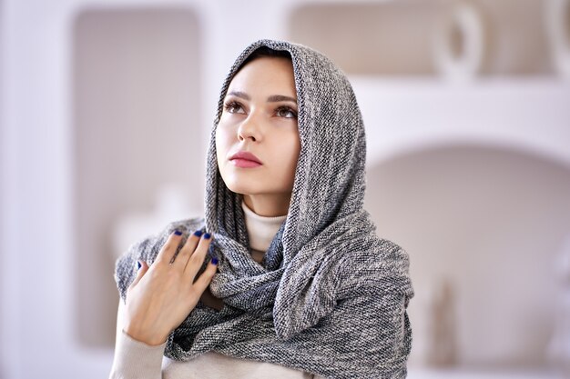 Hijab covers head of sad woman who stands indoors