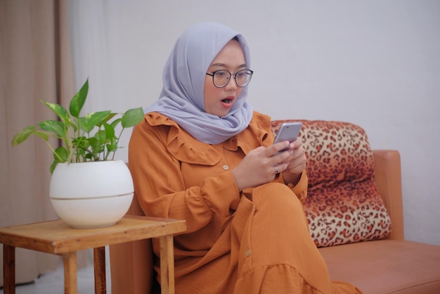 Hijab vrouw met geschokt gezicht terwijl ze naar het telefoonscherm kijkt