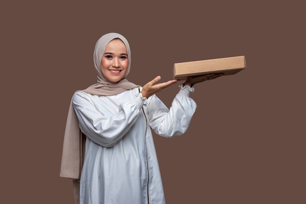 Photo hijab woman holding a pizza box with one left hand and her right hand pointing while smiling