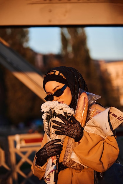 スタイリッシュなサングラスとエレガントなフランスの衣装を着たヒジャブの女性が夕暮れ時に街を歩いています