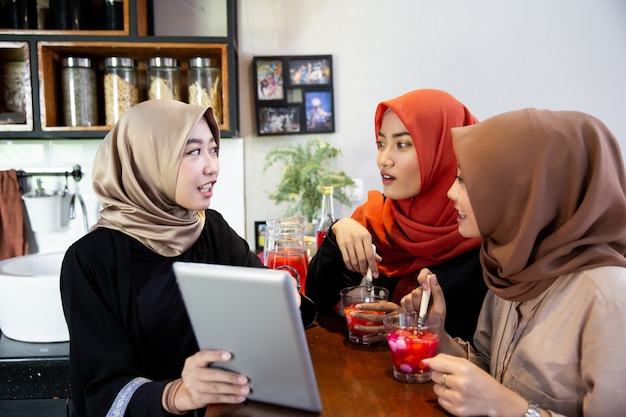 히잡을 기다리는 동안 디지털 태블릿을 사용하는 여자와 친구