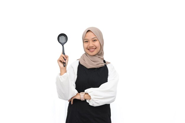 Hijab young girl in black apron holding cooking utensil on white background