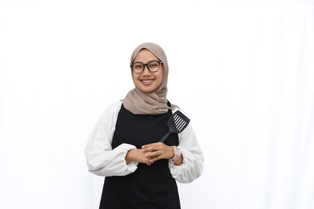 Hijab young girl in black apron holding cooking utensil on white background