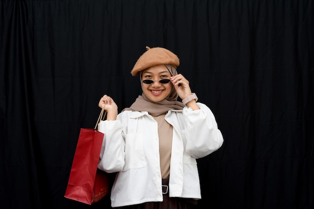 Photo hijab young girl with shopping bag and expensive glasses on black background