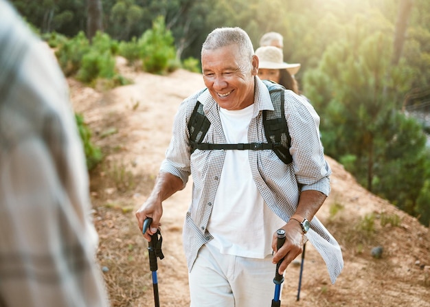 Hike trekking sticks and senior male walking with friends for fitness and health in nature Healthy active and smiling mature man hiking with a backpack Old group on an outdoor wellness adventure