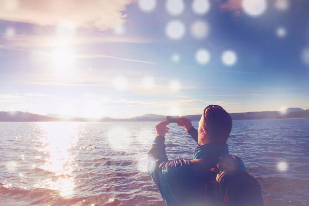 写真 海岸でハイカーがスマートフォンで写真を撮る 静かな湾の静かな水位 抽象的なフレア
