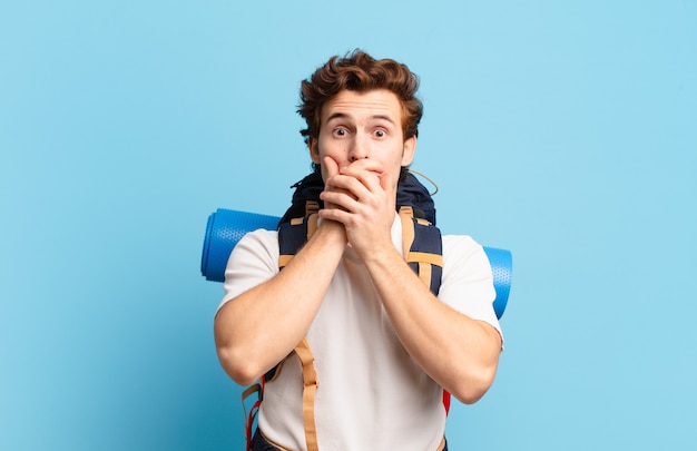 Hiker boy covering mouth with hands with a shocked, surprised expression, keeping a secret or saying oops