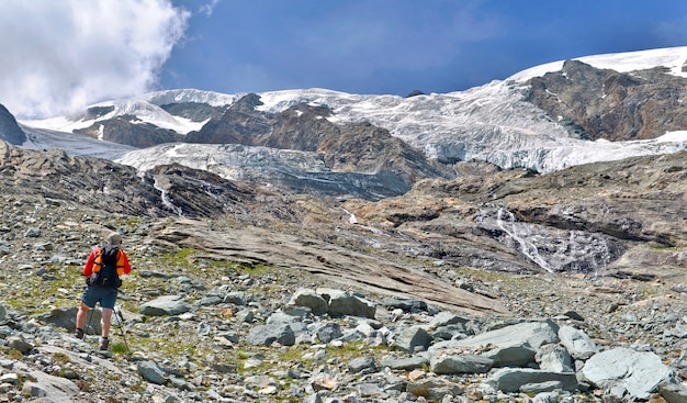 Hiker climbing rocky mountain to a glacier in summer