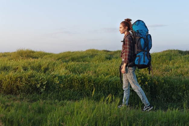 Hiker girl is traveling with a backpack on the landscape background