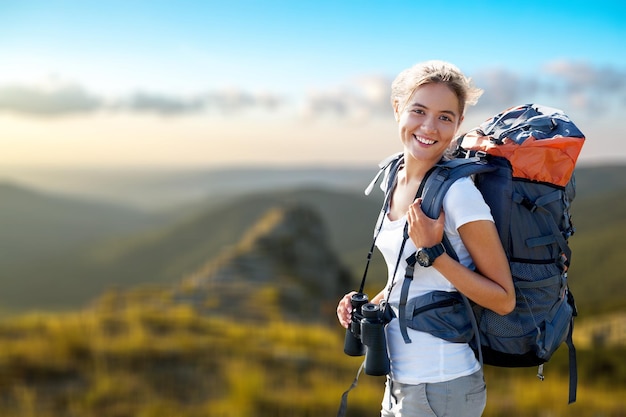 Hiker Looking In Binoculars Enjoying Spectacular View On Mountain Top Above The Clouds