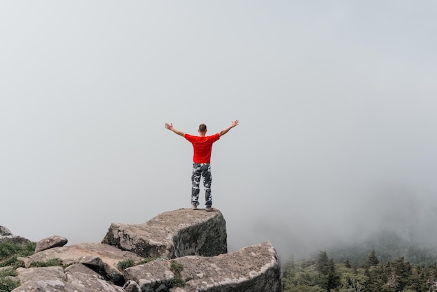 写真 山の頂上にいるハイカーの男は、雲の上に手を上げて空中写真を楽しんでいますピダン山