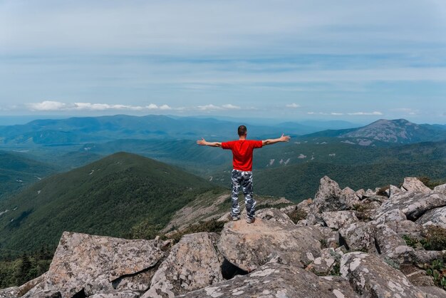 Hiker man on the top of the mountain enjoys the aerial view raising his hands above the clouds Mount Pidan