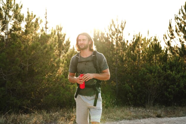 Photo hiker man with backpack holding thermos in his hand