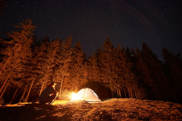 Hiker near campfire and tourist tent at night