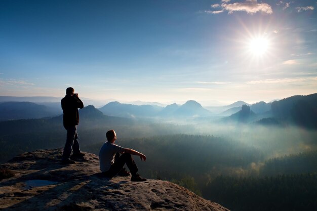 Photo hiker and photo enthusiast stay with tripod on cliff and thinking dreamy fogy landscape blue mist
