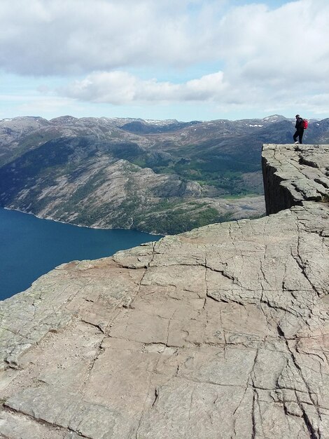 Hiker standing on cliff by lake against cloudy sky