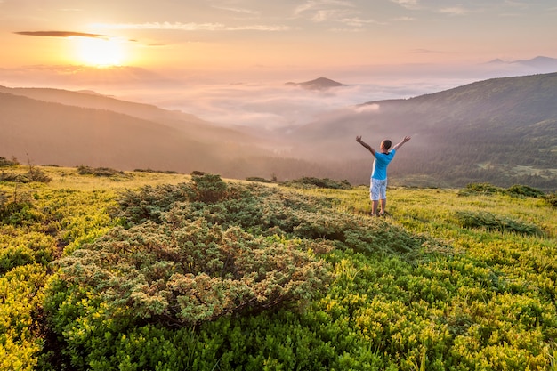 Hiker standing on top of a mountain with raised hands and enjoying sunrise