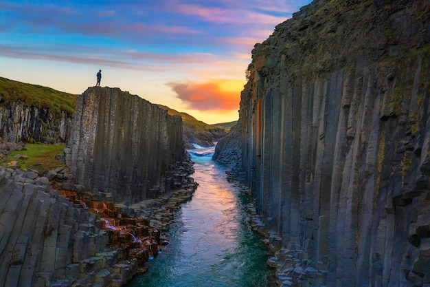 Hiker standing at the top of studlagil canyon in iceland at sunset