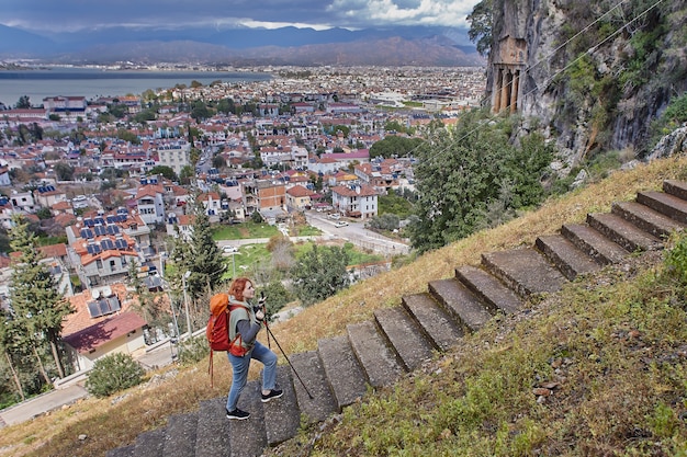 Hiker with backpack and trekking poles climbs stairs to amyntas rock tombs of telmessos ancient city in fethiye turkey in early spring