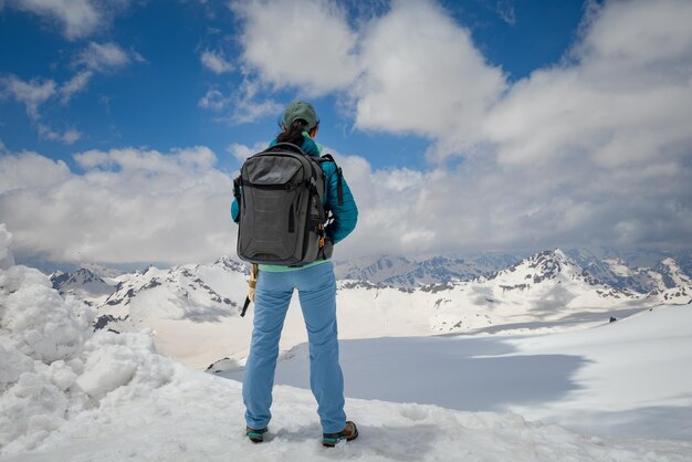 トップを達成するために立っているハイカーの女性。雪山を眺める。