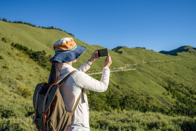 산책하는 여성이 휴대전화를 사용하여 산 위에서 사진을 찍습니다.