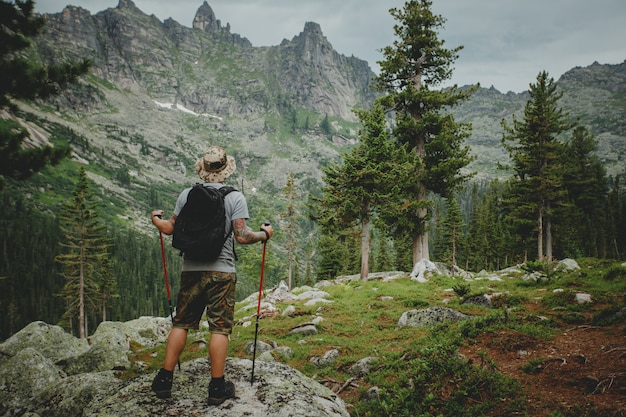 バックパックと崖のトレッキングと夏の屋外で山を見てハイカーの若い男