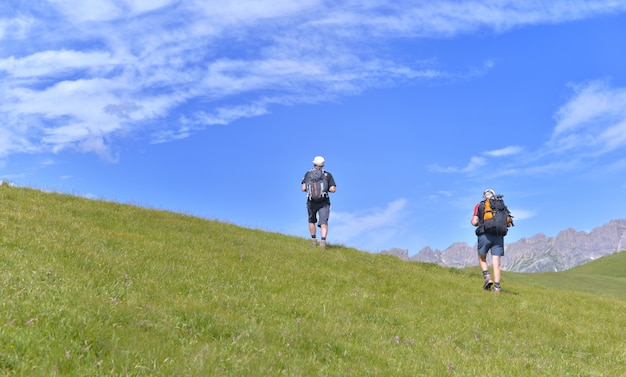 Hikers climbing a grassy hill in alpine mountain under blue sky