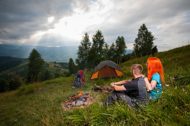 hikers on green grass near campfire, tent