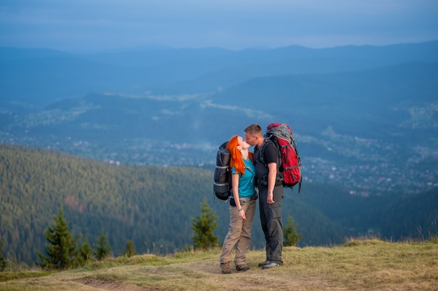 Viandante ragazzo e donna dai capelli rossi che bacia sulla strada in montagna