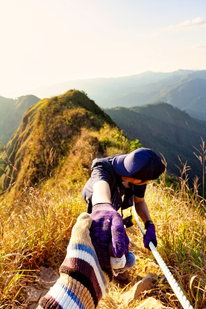 Hikers hold hand helping each other hardly climb mountain.