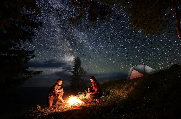 Hikers near campfire and tent at night camping