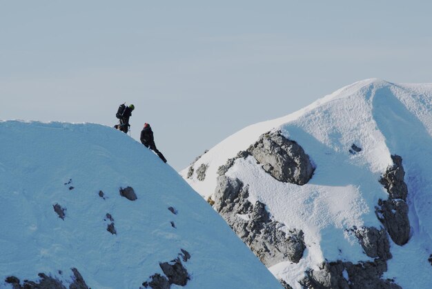 Hikers resting on snowcapped mountain against sky during sunny day