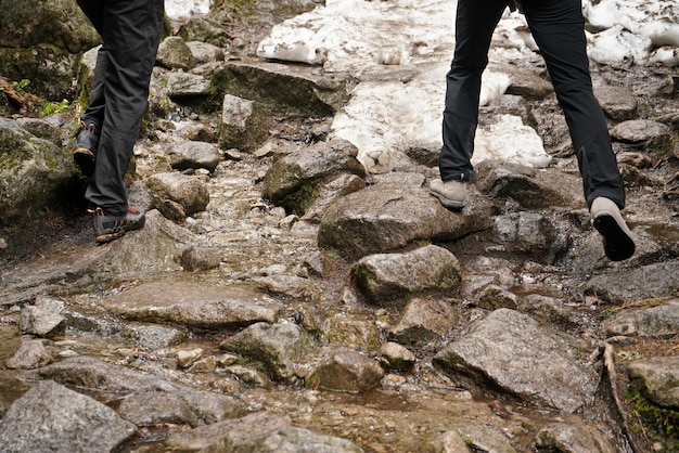 Путешественники, идущие по лесу, детали их ботинок / туфель ступают по мокрым камням, некоторые из них все еще покрыты снегом.