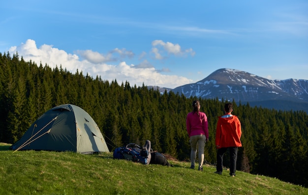 hikers with backpacks on top of a hill near tents