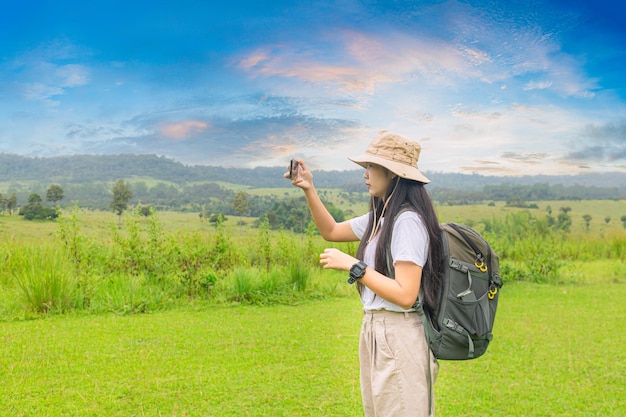 ハイキングバックパックの女性スマートフォンで美しい景色の写真を撮るバックパックを持つ女性